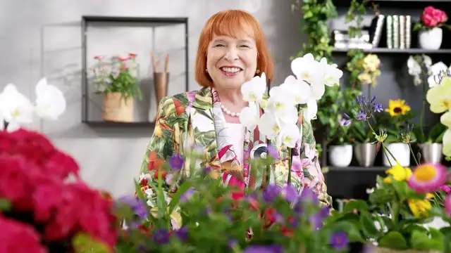 Ingrid Hofmann, Geschäftsführerin, im floralen Blazer steht in blumig dekoriertem Raum.