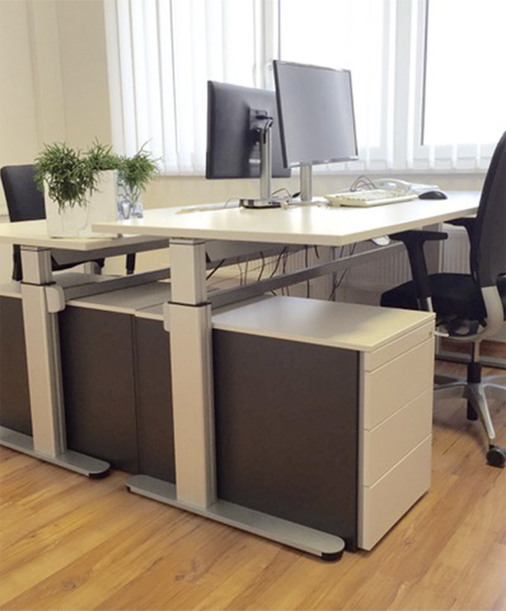 Heller Büroarbeitsplatz mit höhenverstellbarem Schreibtisch, Monitoren und ergonomischem Stuhl.