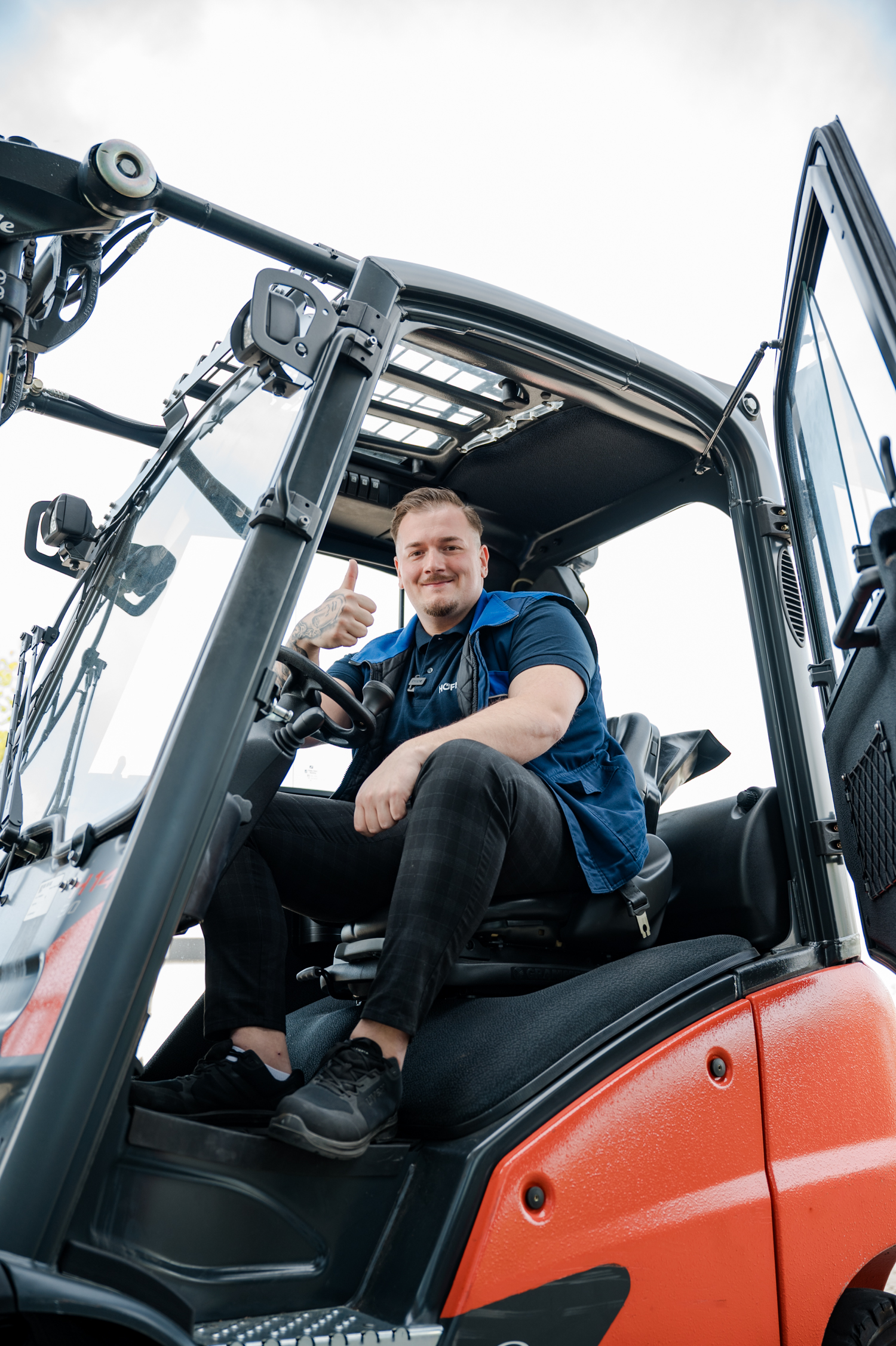 Zeitarbeitsmitarbeiter fährt Gabelstapler und zeigt Daumen hoch im Außenbereich